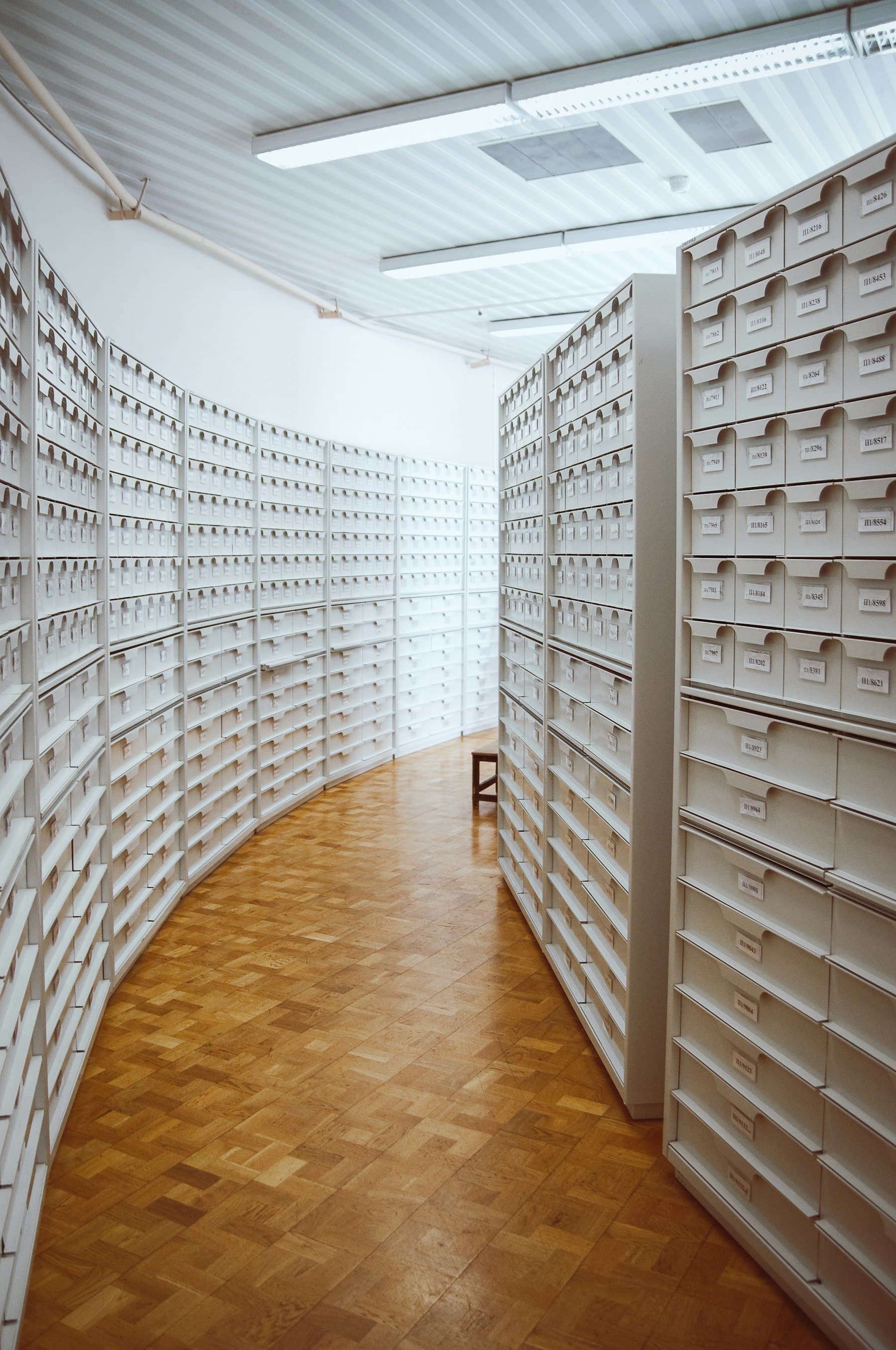 A curved corridor lined floor to ceiling with white, labelled archive drawers.