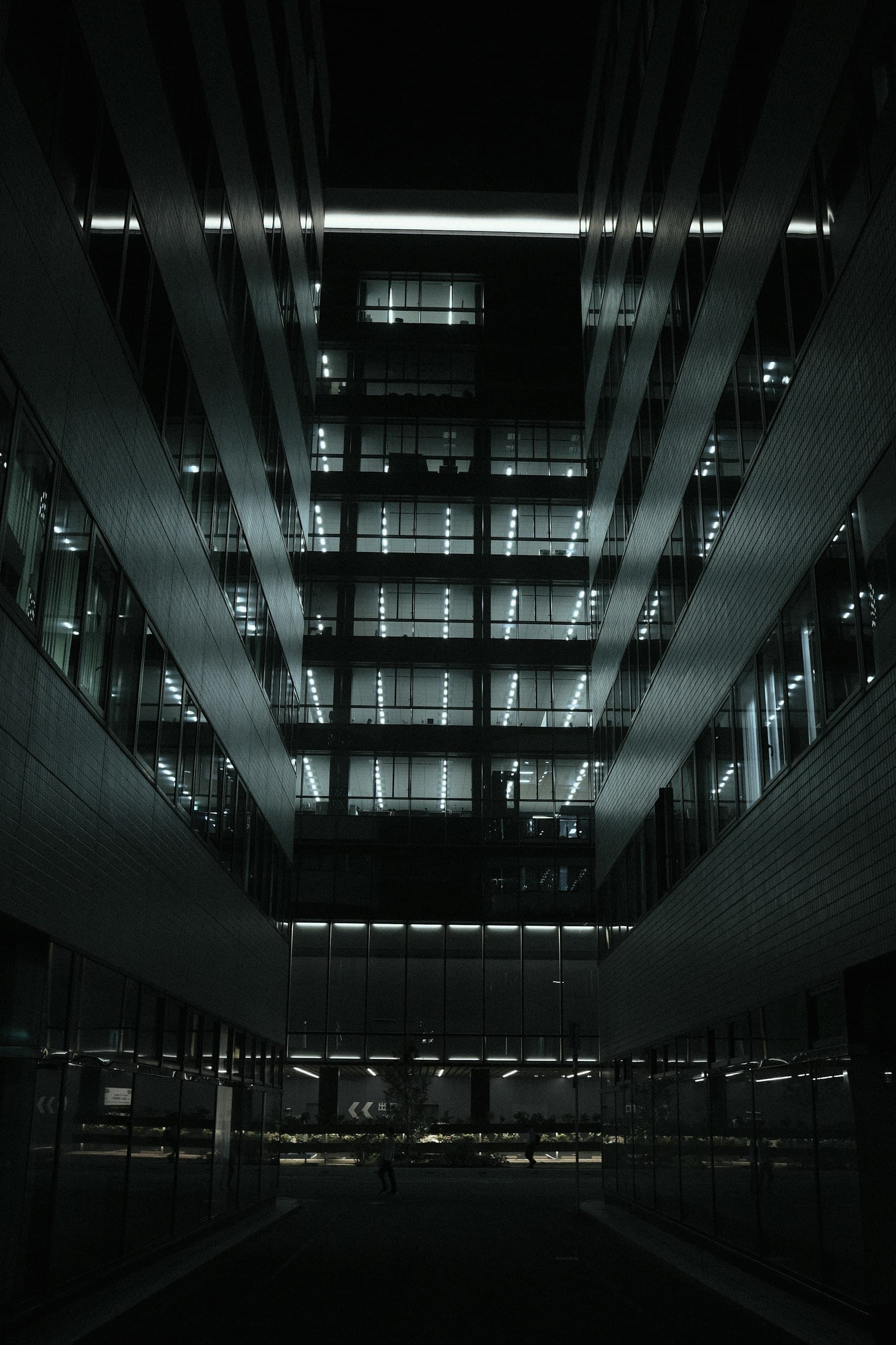 A contemporary office building at night: a symmetrical facade of lit glass floors between dark stone wings.