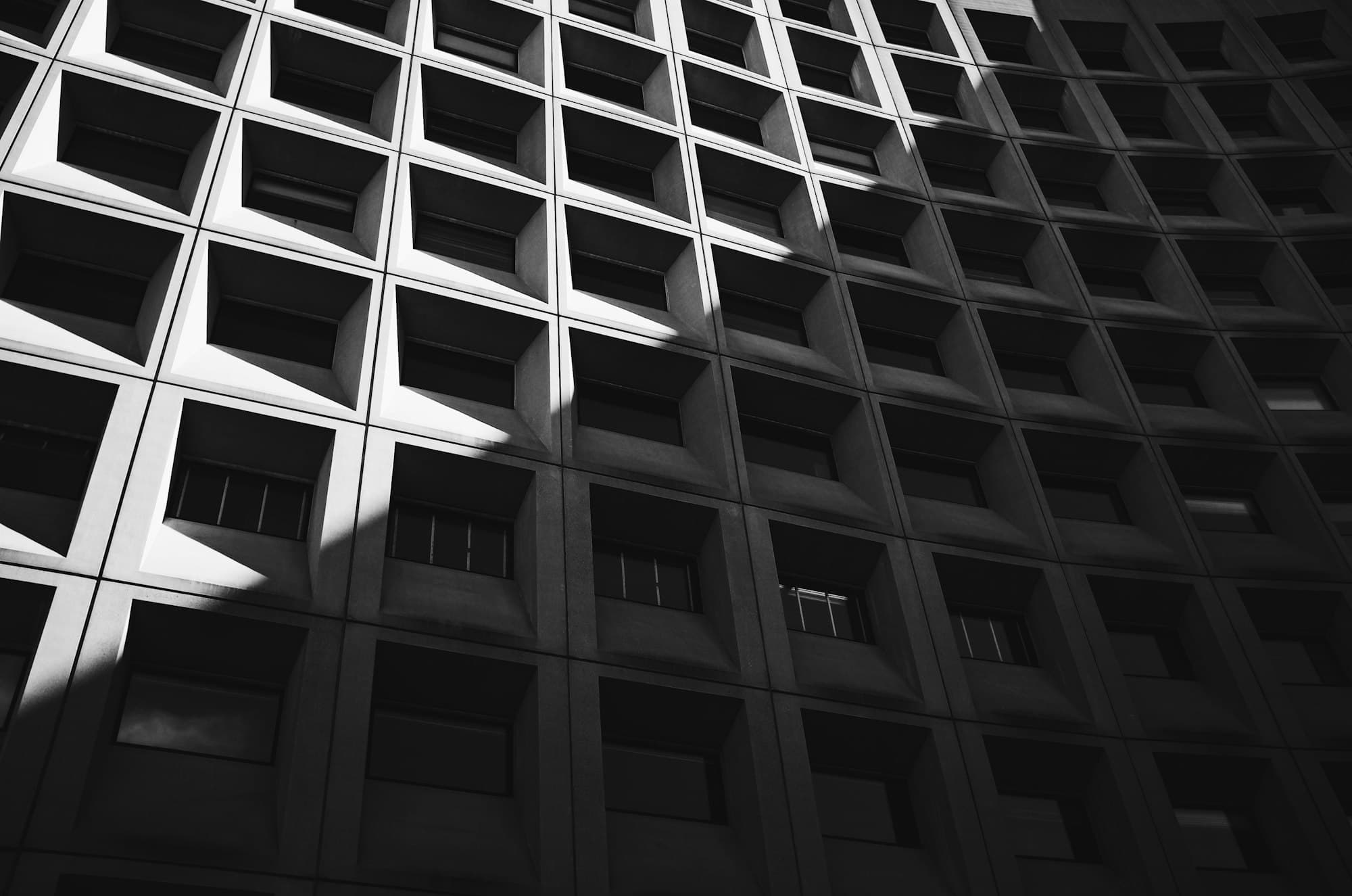A concrete building facade of deep, repeating window frames catching raking light.
