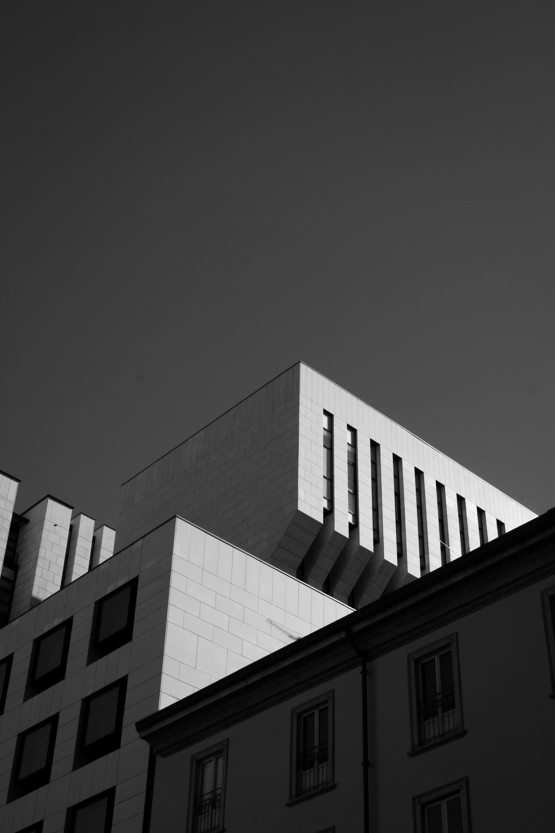 The sharp corner of a pale stone building with vertical window slots, seen from below.